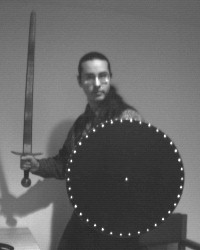 Here I am wielding one of my older swords (I bought itat the MD RenFest many years ago), as well as a shieldthat I recently made (20" wooden shield, black w/ silvery studs).